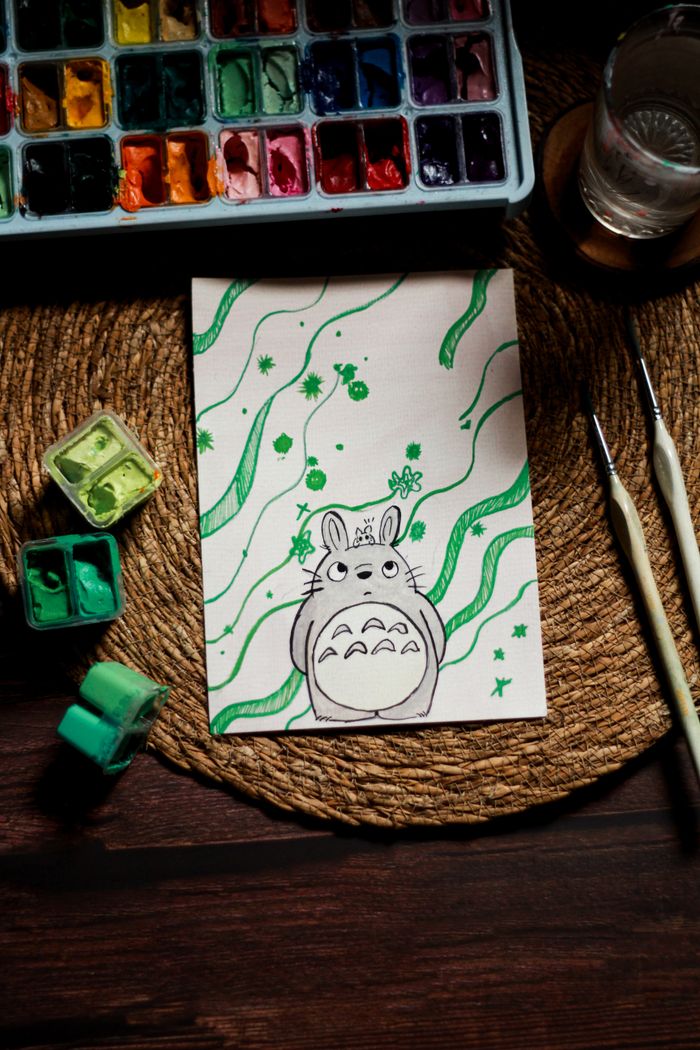 our-story-02 Charming Totoro sketch surrounded by watercolors and brushes, perfect for art enthusiasts.